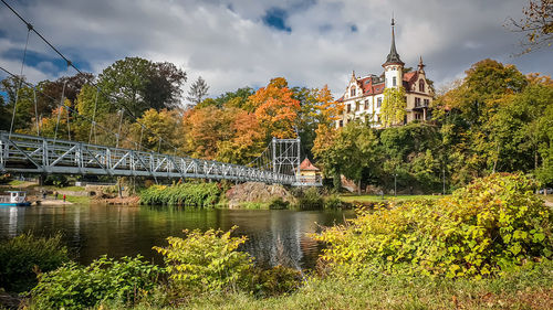 Bridge over river amidst trees and buildings against sky