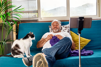 Bearded knitting scarf and playing with his cat as part of his hobby