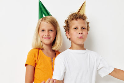 Happy girl and boy wearing party hat standing against white background