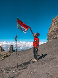 Rear view of man standing on mountain against blue sky