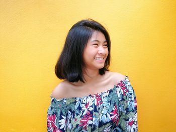 Smiling teenage ball looking away against yellow wall