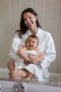 Mother in a bathrobe and with a child standing in the bathroom