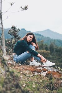 Portrait of young woman sitting on tree against mountain