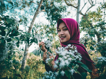 Portrait of smiling young woman against plants and trees