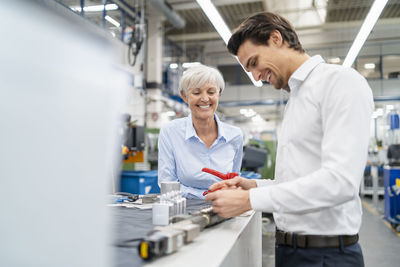 Happy businessman and senior businesswoman examining workpiece in a factory