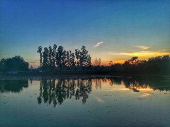 Silhouette trees by lake against sky during sunset