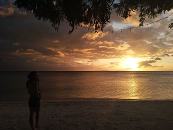 Rear view of woman standing on beach against sky during sunset