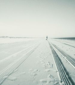 Tire tracks on snow covered land against clear sky