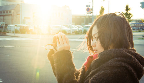 Side view of woman photographing with camera during sunny day in city