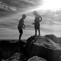 Brothers standing on rocks against sky