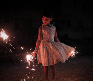 Girl holding sparklers while standing at night