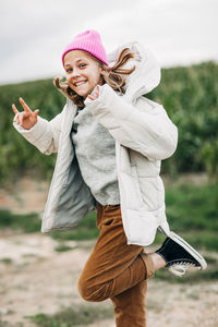 Cheerful beautiful teenage girl in a yellow raincoat and pink hat jumping against the background 