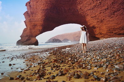 Full length of woman standing against rock formation at beach