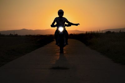 Rear view of silhouette man standing on street during sunset