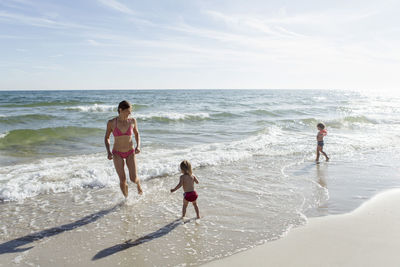 Mother and daughters enjoying on beach against sky during sunny day