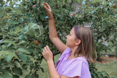 Side view of young woman standing against plants