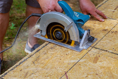 Low section of man using circular saw on wood