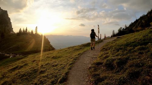 Rear view of woman walking on landscape against sky during sunset