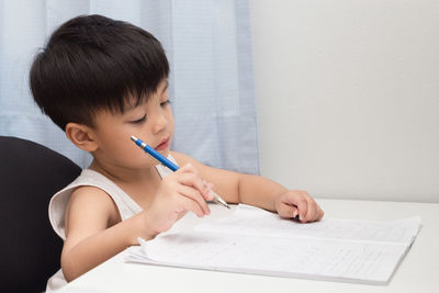 Close-up of boy writing in book at table