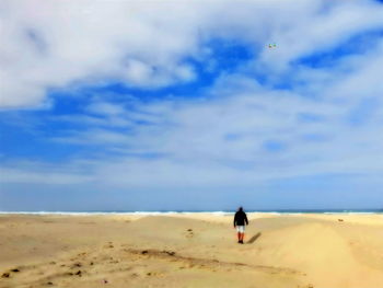 Woman on sand dune at beach against sky