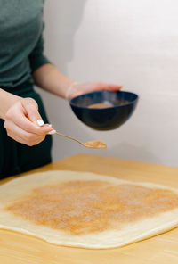 One caucasian young girl sprinkles cinnamon sugar on the dough on the table.