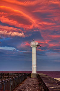 Lighthouse by sea against sky during sunset