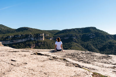 View of behind of woman wearing a white t-shirt sitting relaxed on a table enjoying the scenery