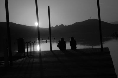 Silhouette people sitting by lake against sky