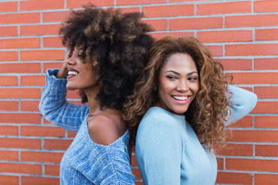 Portrait of attractive women with curly hair and afro hair smiling against brick wall beauty concept