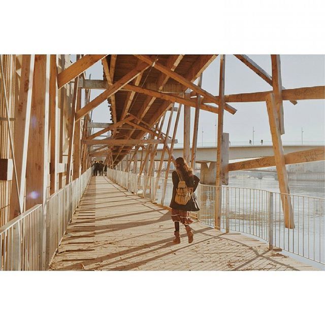 full length, lifestyles, leisure activity, transfer print, built structure, architecture, casual clothing, rear view, auto post production filter, railing, walking, standing, wood - material, bridge - man made structure, young adult, connection, day, men