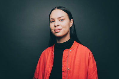 Portrait of woman smiling while wearing orange jacket over gray background