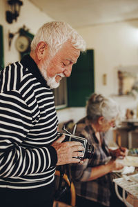 Senior man examining camera by woman painting at home