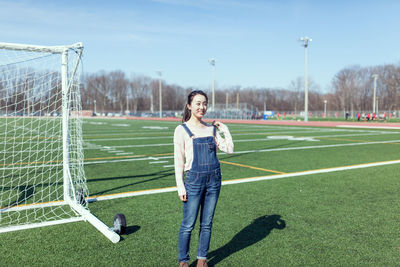 Smiling young woman standing by goal post on multi-purpose stadium