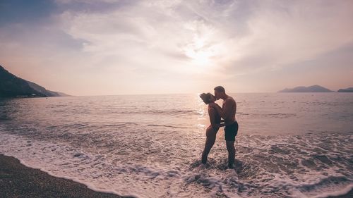 Friends on beach against sky during sunset