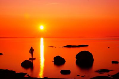 Silhouette people standing by sea against orange sky during sunset