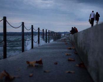 People on retaining wall by sea against sky