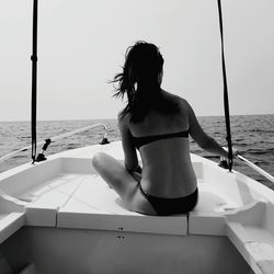 Rear view of bikini woman sitting on boat sailing in sea