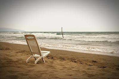 Empty chair on beach against clear sky