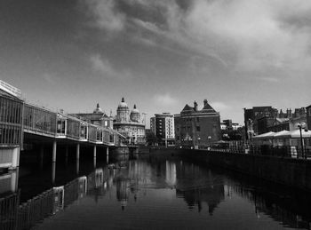 Canal by buildings in city against sky