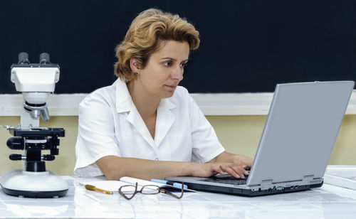 Mid adult woman using smart phone while sitting on table