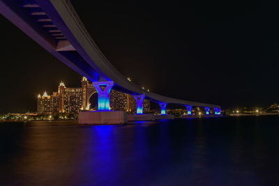 Illuminated bridge over river against buildings at night