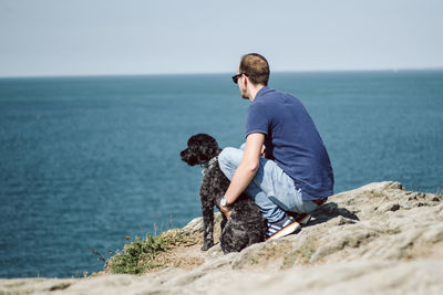 Rear view of dog sitting on cliff against sea