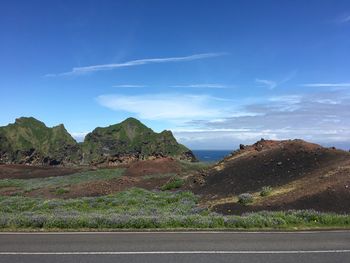 Scenic view of road by mountains against blue sky