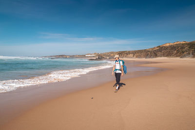 Rear view of woman walking at beach against sky