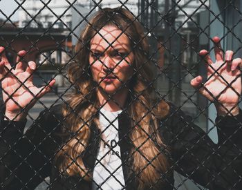 Close-up portrait of young woman looking through fence