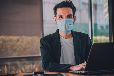 Man wearing mask using laptop at table