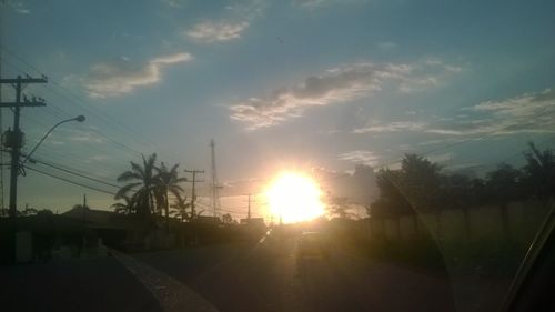 Silhouette road by electricity pylon against sky during sunset