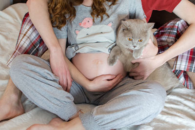 Midsection of pregnant woman with cat and man sitting on bed