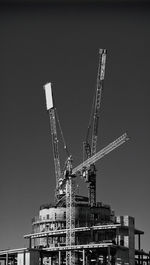 Low angle view of crane by building against clear sky