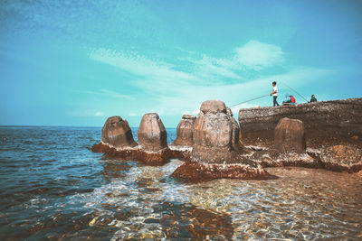 Man on rocks by sea against blue sky